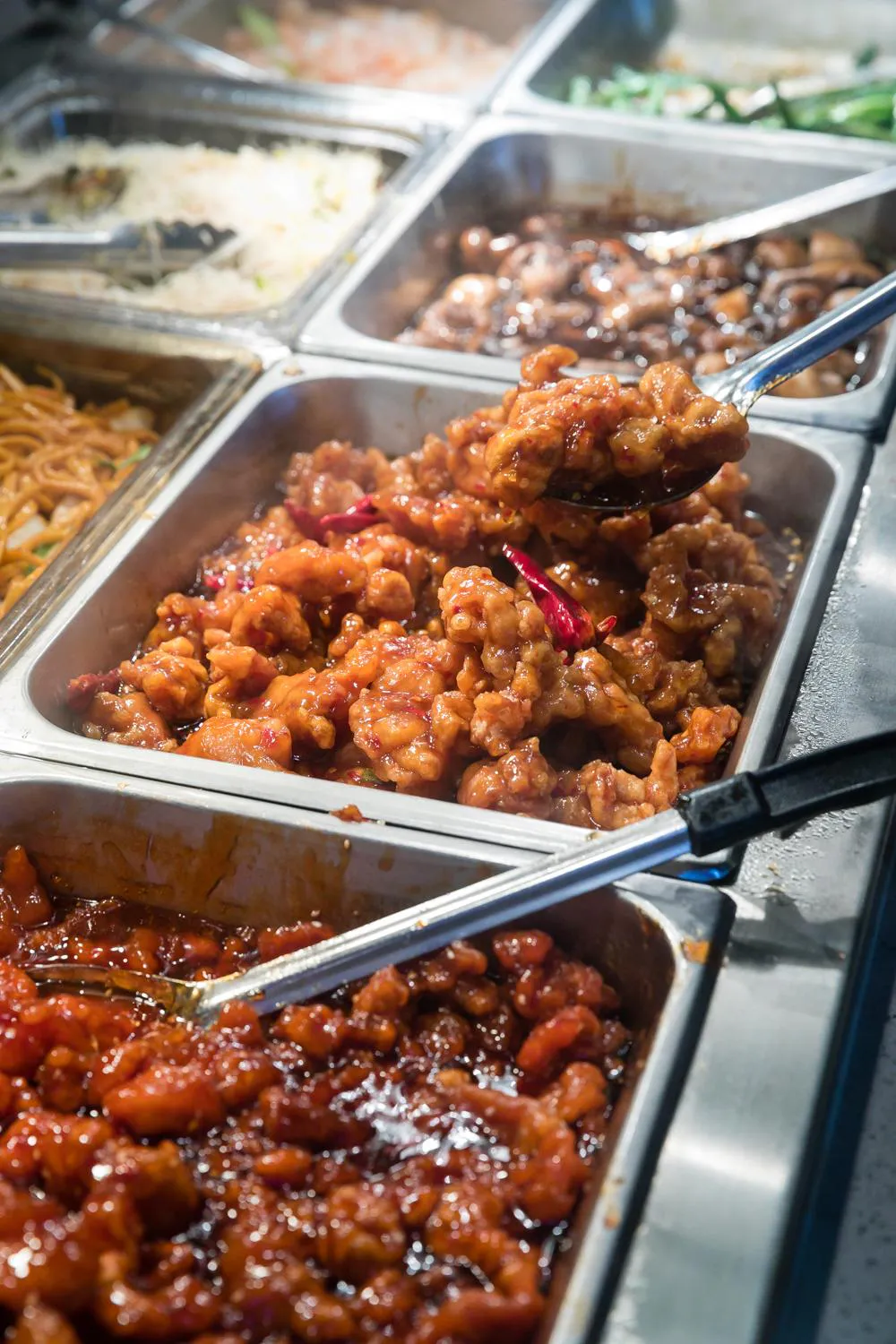 Buffet trays filled with sweet and spicy chicken, noodles, rice, and vegetables