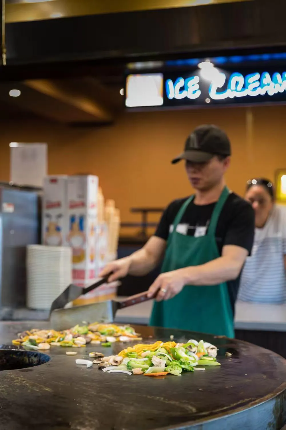 Chef cooking vegetables and noodles on a flat-top grill at a buffet restaurant