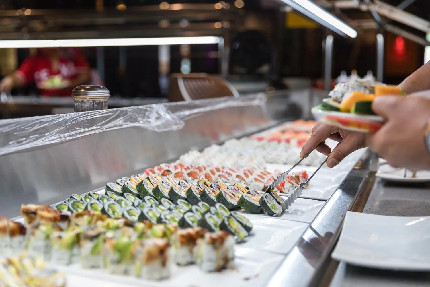 Hand selecting a sushi roll from rows of assorted rolls at a buffet