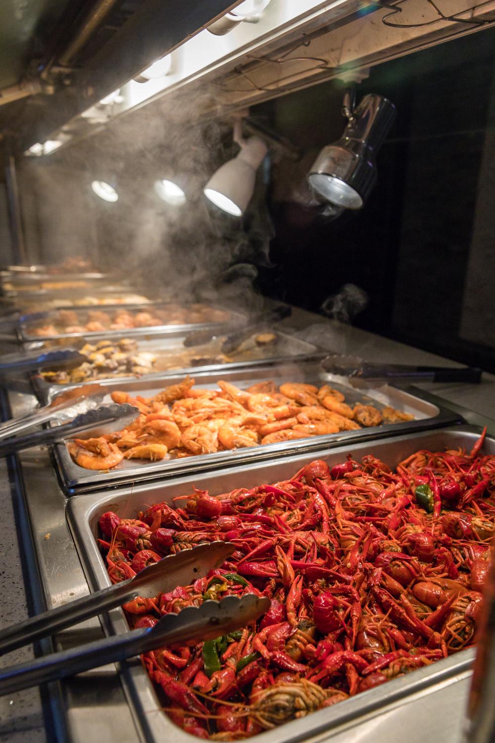 Steaming buffet trays of crawfish, shrimp, and other seafood dishes